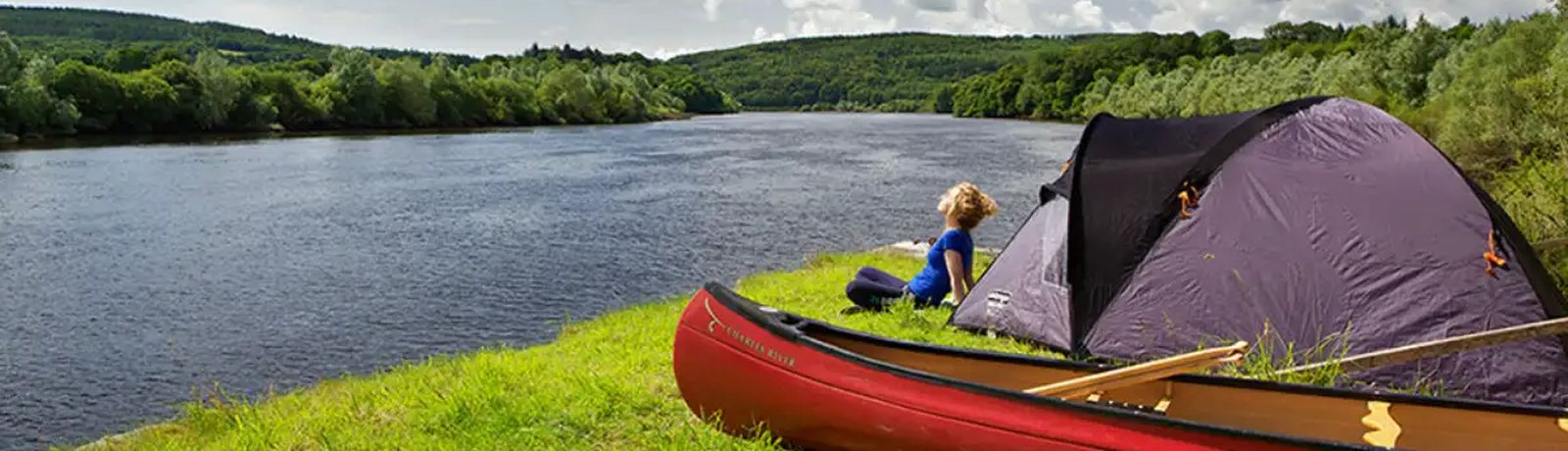 A canoe and tent pitched on the riverbank, with someone sitting looking out over the water