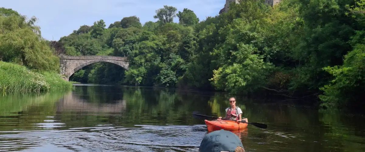 A kayaker smiling on the river, with the old bridge and Lismore Castle behind